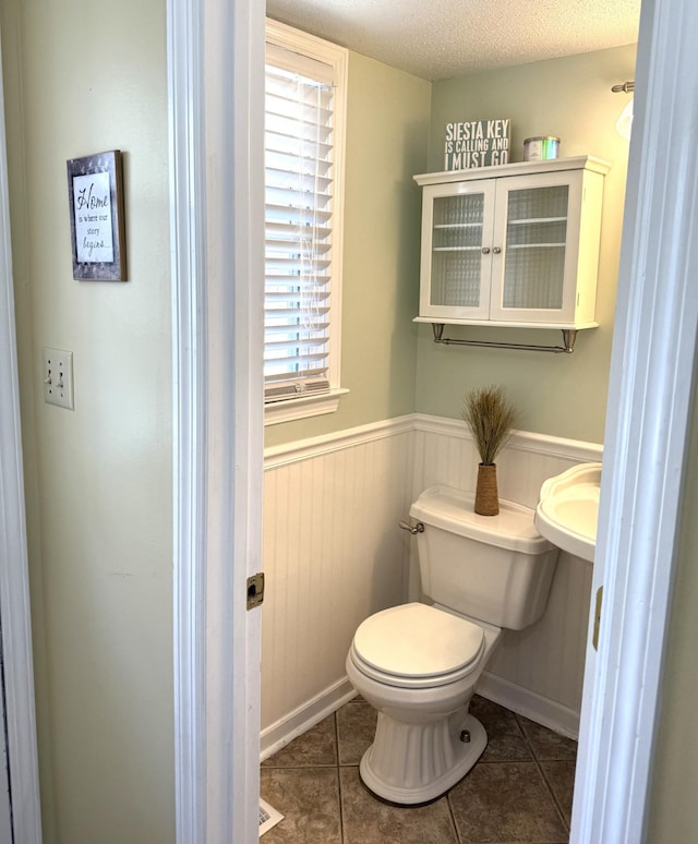 bathroom featuring toilet, tile patterned flooring, a wainscoted wall, and a textured ceiling