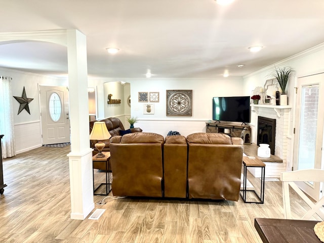 living room featuring ornamental molding, plenty of natural light, light wood finished floors, a wainscoted wall, and a brick fireplace