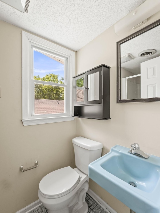 bathroom with baseboards, a sink, toilet, a textured ceiling, and tile patterned flooring