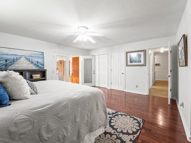 bedroom with wood finished floors, multiple closets, baseboards, ceiling fan, and a textured ceiling