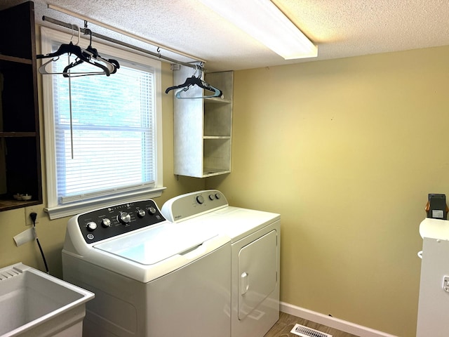 laundry area featuring washing machine and dryer, a textured ceiling, healthy amount of natural light, and baseboards