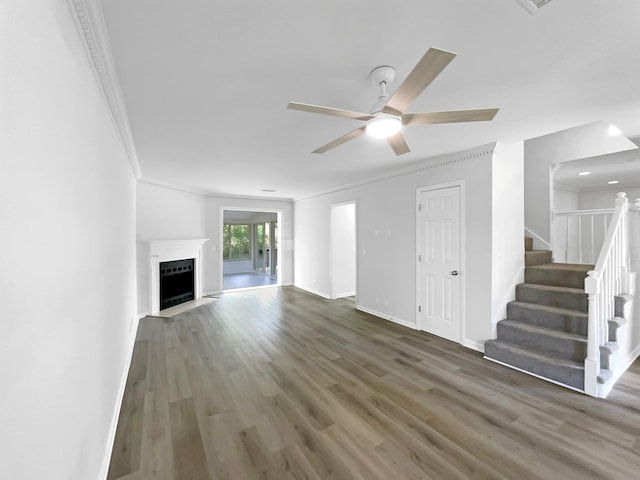 unfurnished living room featuring crown molding, wood finished floors, ceiling fan, baseboards, and stairs