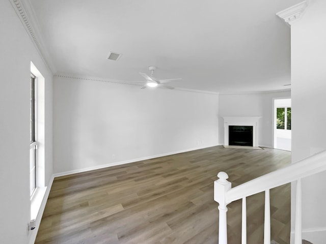 unfurnished living room with wood finished floors, ceiling fan, a fireplace, baseboards, and ornamental molding
