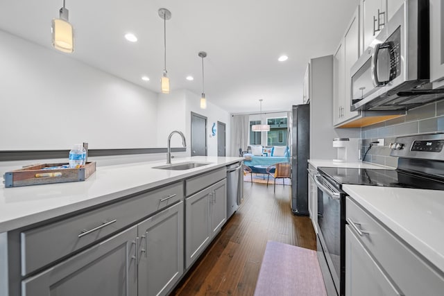 kitchen with appliances with stainless steel finishes, a sink, gray cabinetry, dark wood-style floors, and light countertops