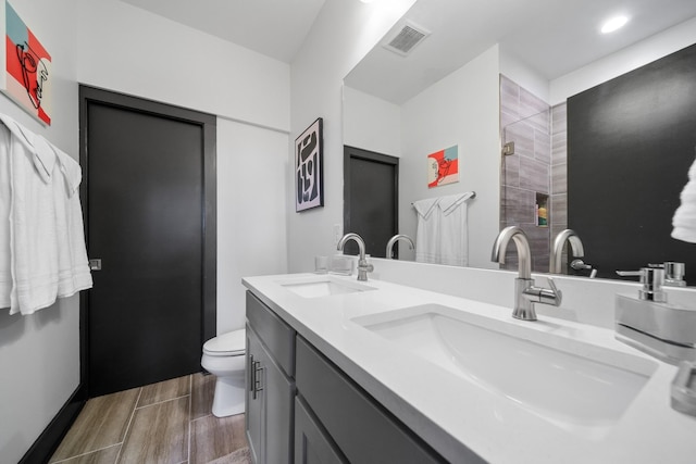 bathroom with tiled shower, toilet, double vanity, and wood tiled floors