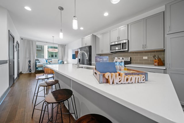 kitchen with appliances with stainless steel finishes, a sink, decorative backsplash, a kitchen bar, and dark wood-type flooring