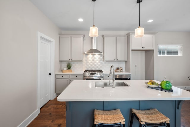 kitchen featuring stainless steel gas range oven, wall chimney range hood, a sink, a kitchen breakfast bar, and tasteful backsplash