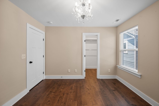 unfurnished dining area featuring dark wood-type flooring, a chandelier, and baseboards