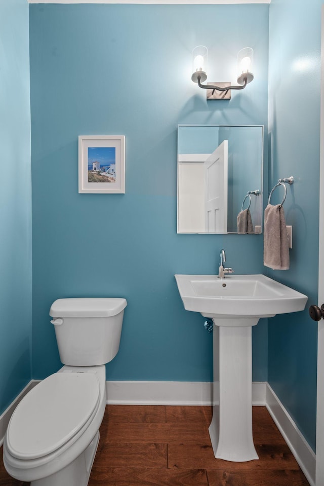 half bath featuring wood finished floors, toilet, and baseboards