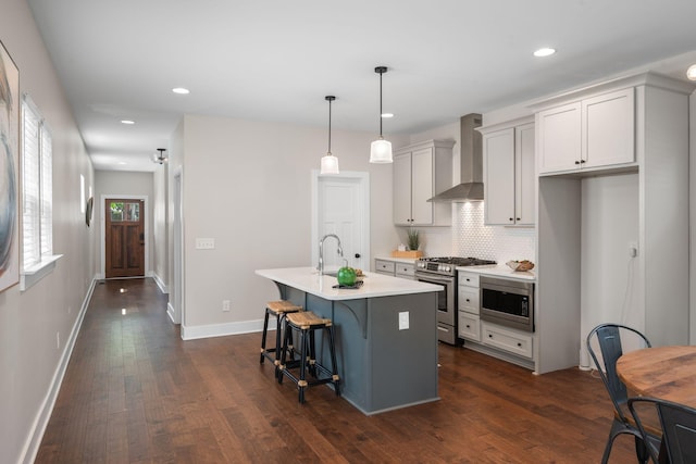 kitchen featuring wall chimney range hood, stainless steel appliances, a kitchen bar, an island with sink, and a sink
