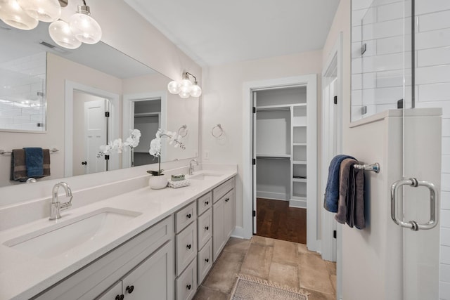 bathroom with a spacious closet, a shower stall, double vanity, and baseboards