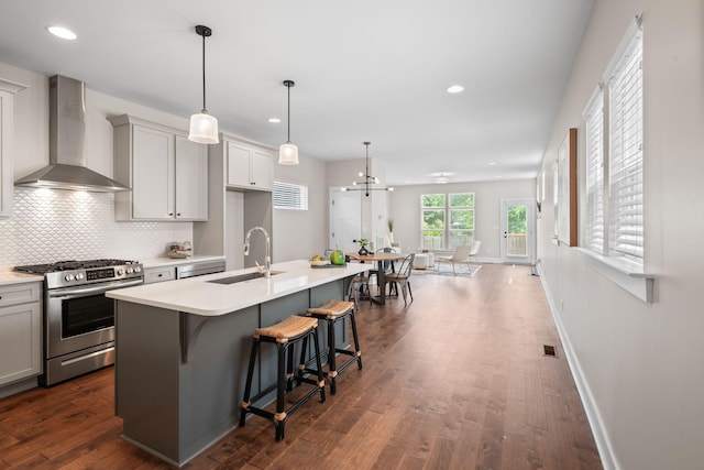 kitchen with a sink, stainless steel gas range, wall chimney range hood, a kitchen breakfast bar, and a kitchen island with sink