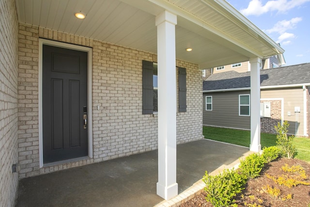 view of exterior entry featuring covered porch and brick siding