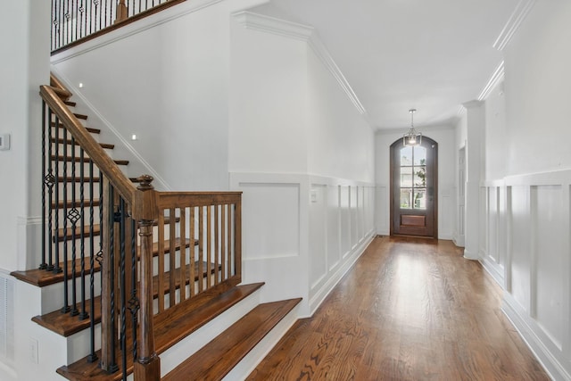 entryway with a decorative wall, stairway, wood finished floors, crown molding, and wainscoting