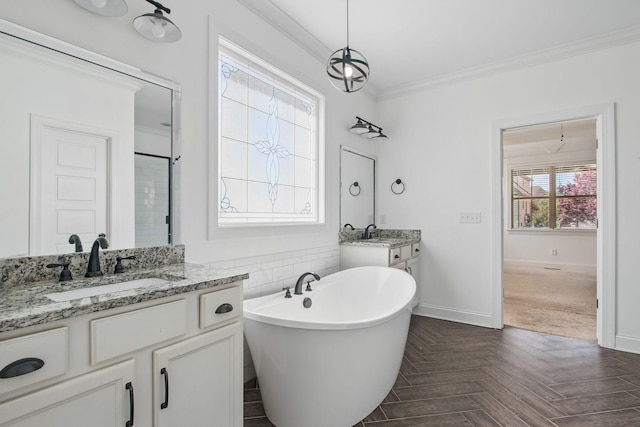 full bathroom with ornamental molding, a freestanding tub, baseboards, a stall shower, and two vanities
