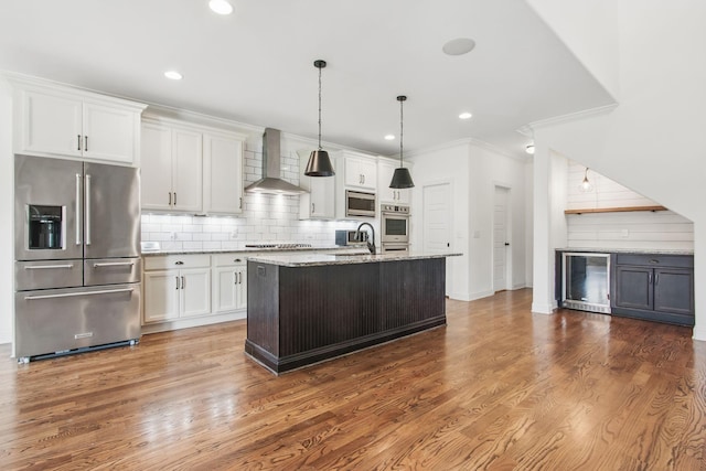 kitchen with stainless steel appliances, wall chimney range hood, wine cooler, a sink, and decorative backsplash