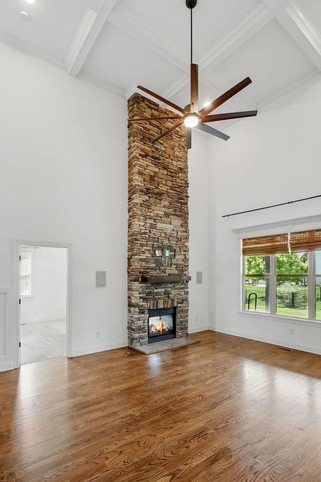 unfurnished living room featuring a towering ceiling, ceiling fan, wood finished floors, beam ceiling, and a fireplace
