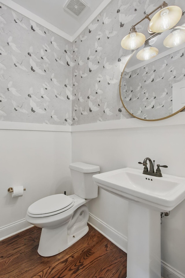 half bathroom featuring wood finished floors, toilet, baseboards, a sink, and ornamental molding