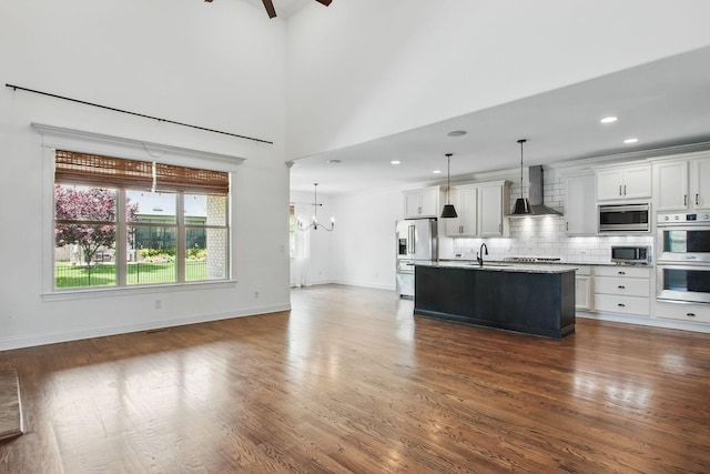 kitchen with wall chimney exhaust hood, stainless steel appliances, decorative backsplash, a chandelier, and dark wood-type flooring