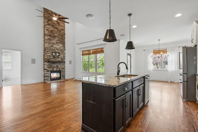 kitchen with appliances with stainless steel finishes, a sink, light wood-style floors, light stone counters, and a towering ceiling