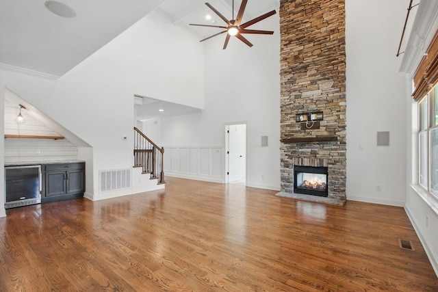 unfurnished living room featuring a ceiling fan, a high ceiling, wood finished floors, stairs, and a stone fireplace