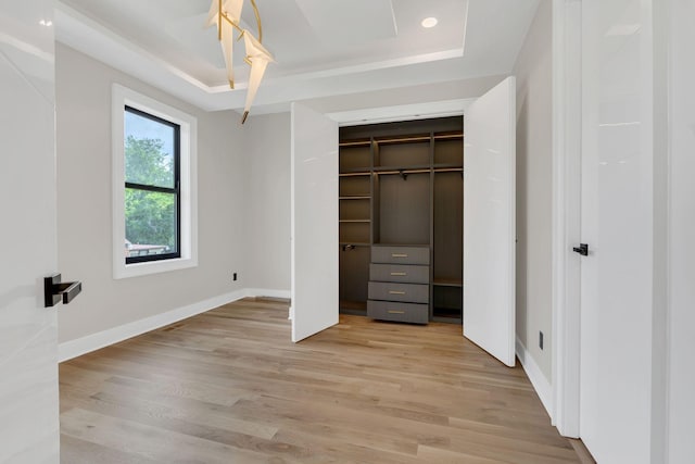 unfurnished bedroom featuring a raised ceiling, light wood finished floors, and baseboards