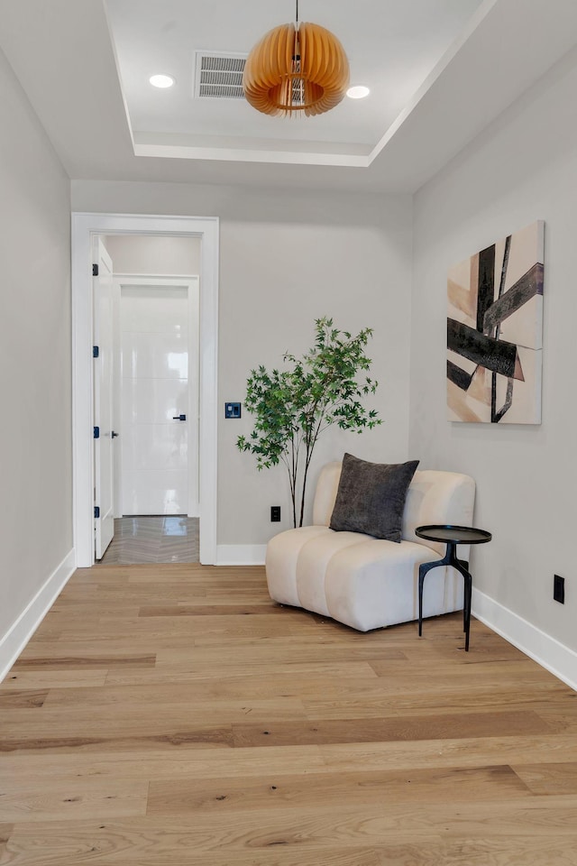 sitting room featuring baseboards, a raised ceiling, and light wood finished floors