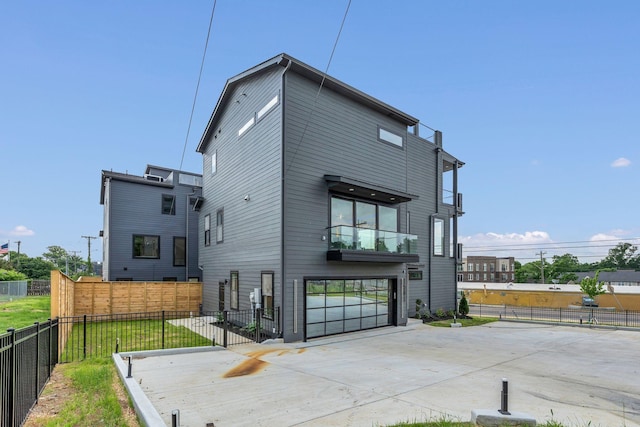 back of house featuring an attached garage, concrete driveway, fence, and a balcony