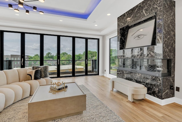 living room featuring healthy amount of natural light, wood finished floors, a raised ceiling, baseboards, and recessed lighting