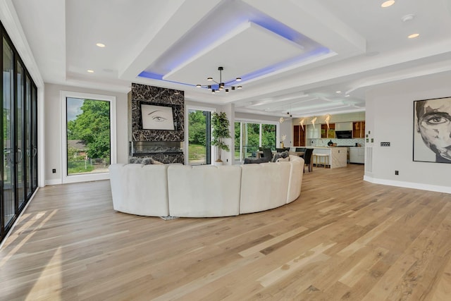 unfurnished living room featuring a tray ceiling, a chandelier, light wood-style floors, baseboards, and recessed lighting