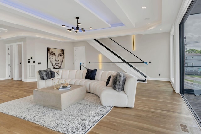 living room featuring a raised ceiling, a chandelier, baseboards, light wood-style flooring, and recessed lighting