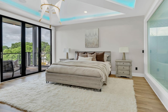 bedroom featuring access to outside, a raised ceiling, light wood finished floors, baseboards, and recessed lighting