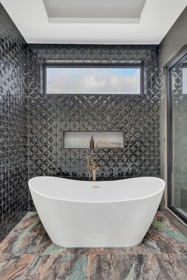 full bathroom with healthy amount of natural light, a soaking tub, and marble finish flooring