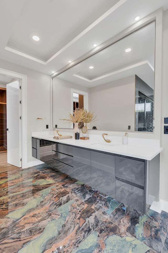 bathroom featuring a tray ceiling, double vanity, baseboards, and recessed lighting
