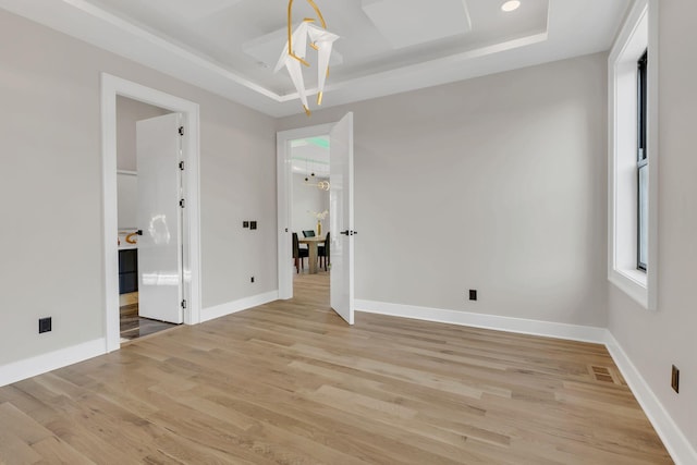spare room featuring a tray ceiling, light wood-style flooring, and baseboards