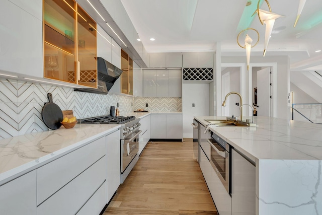 kitchen featuring modern cabinets, stainless steel appliances, a sink, light wood-style flooring, and decorative backsplash