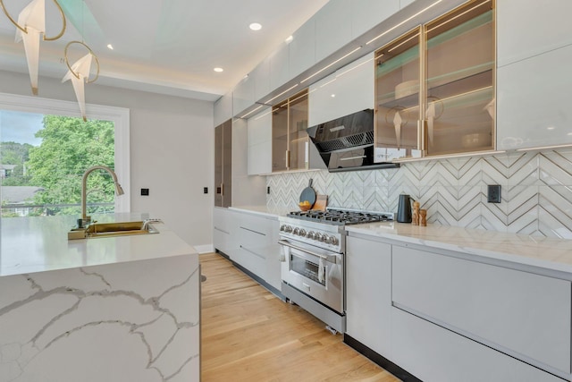 kitchen featuring stainless steel stove, modern cabinets, a sink, recessed lighting, and tasteful backsplash
