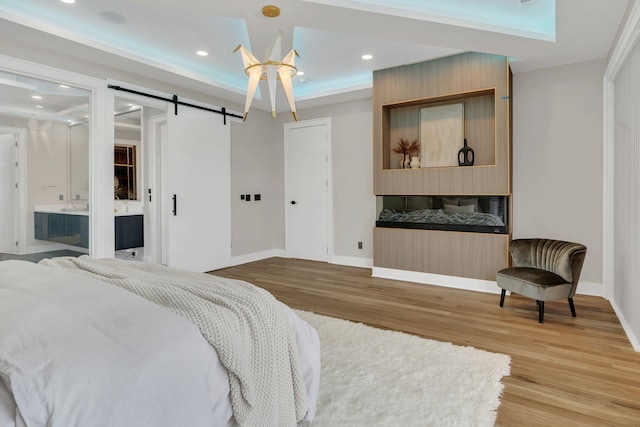 bedroom featuring light wood-type flooring, baseboards, a barn door, and recessed lighting