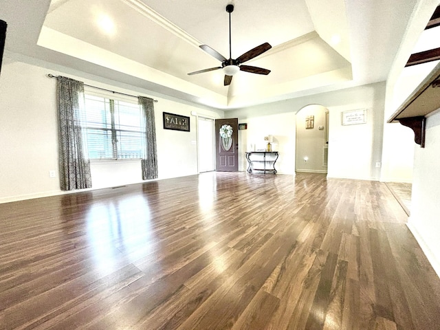 unfurnished living room featuring a tray ceiling, a ceiling fan, arched walkways, and wood finished floors