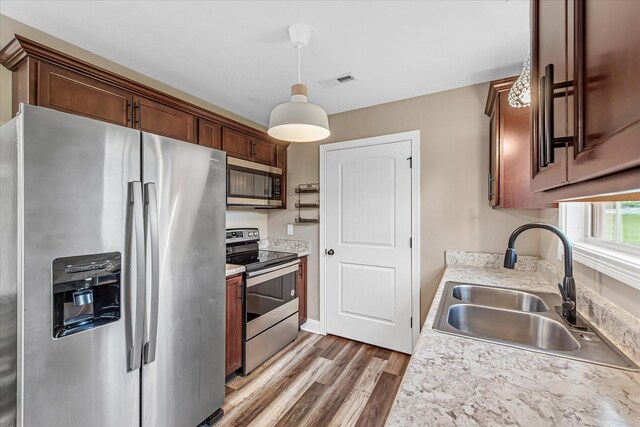 kitchen with appliances with stainless steel finishes, a sink, light wood-style flooring, light countertops, and pendant lighting