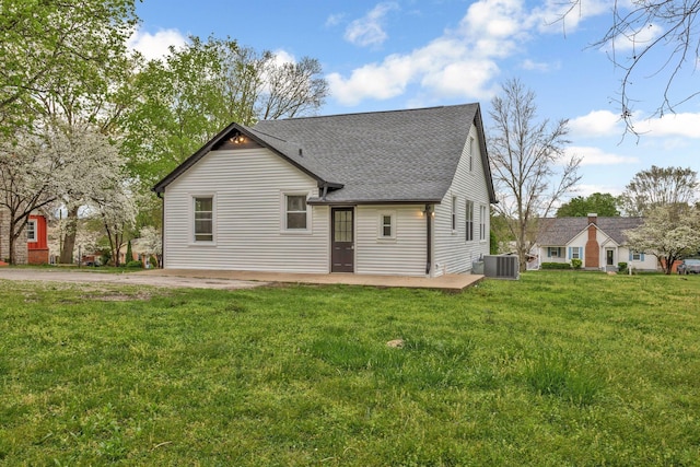 rear view of property featuring cooling unit, a shingled roof, and a yard