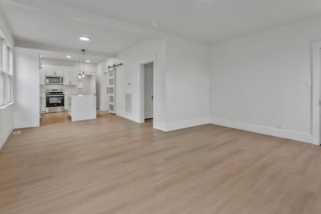 unfurnished living room with a barn door, baseboards, light wood-style floors, and recessed lighting
