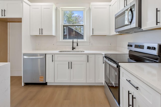 kitchen with stainless steel appliances, a sink, light wood-style flooring, and white cabinets