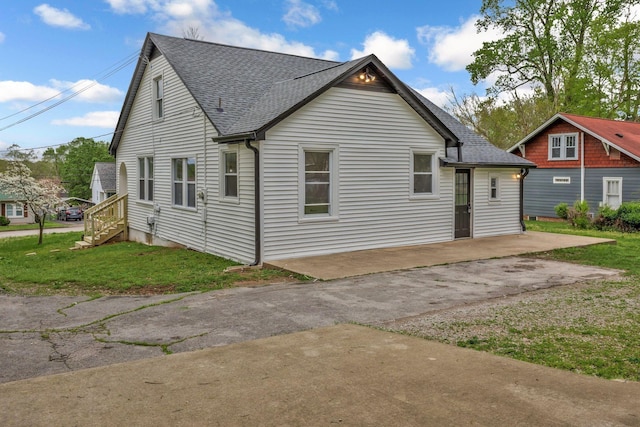 rear view of house featuring roof with shingles, a patio area, and a yard