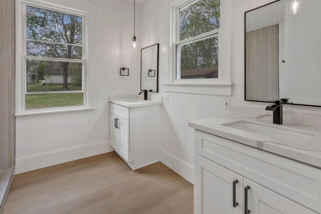 full bathroom featuring wood finished floors, two vanities, and baseboards