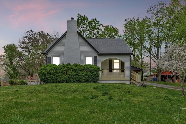 view of front facade with covered porch, a chimney, a front lawn, and a shingled roof