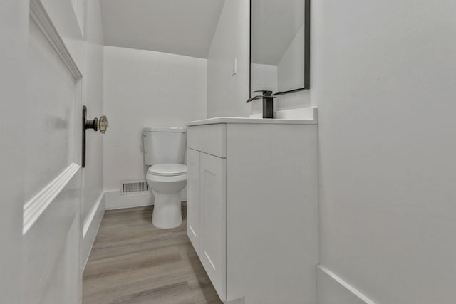 bathroom with toilet, vanity, wood finished floors, and baseboards