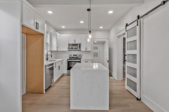 kitchen featuring appliances with stainless steel finishes, a barn door, a kitchen island, a sink, and light wood-style flooring