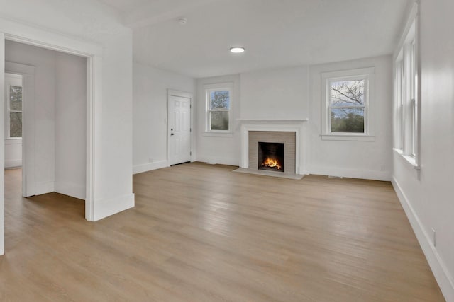 unfurnished living room featuring baseboards, healthy amount of natural light, a fireplace with flush hearth, and light wood finished floors