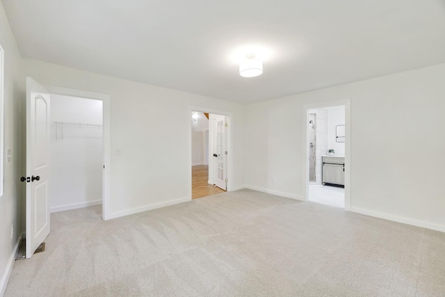 unfurnished bedroom featuring a walk in closet, light colored carpet, baseboards, and a closet